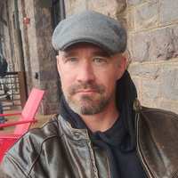 Benjamin Hodgens, wearing a flat cap and leather jacket